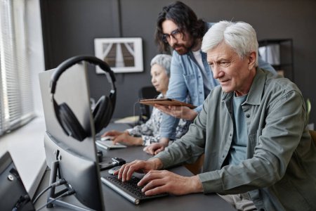 Téléchargez les photos : Portrait latéral d'un homme âgé utilisant un ordinateur en classe avec l'aide d'un instructeur masculin, espace de copie - en image libre de droit