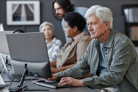 Téléchargez les photos : Portrait latéral d'un homme âgé aux cheveux blancs utilisant un ordinateur dans une école de technologie pour personnes âgées, espace de copie - en image libre de droit