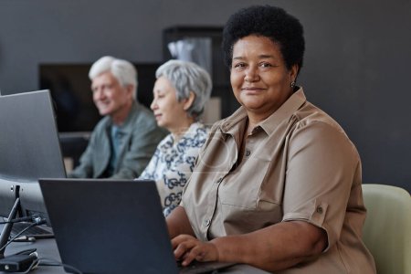 Foto de Retrato de mujer mayor negra en clase de informática para ancianos sonriendo a la cámara, espacio para copiar - Imagen libre de derechos
