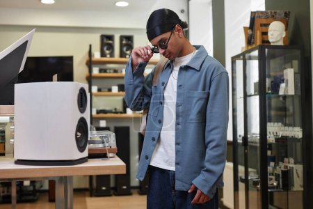 Téléchargez les photos : Portrait latéral de jeune homme noir regardant des haut-parleurs dans un magasin de musique, espace de copie - en image libre de droit