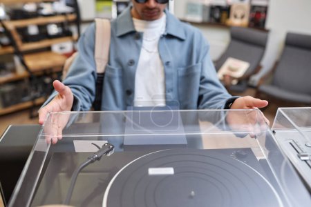 Téléchargez les photos : Gros plan de jeune homme noir ouvrant couvercle pn lecteur de disques dans le magasin de musique, espace de copie - en image libre de droit