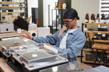 Foto de Retrato de vista lateral del joven negro que elige el reproductor de discos en la tienda de música, espacio para copiar - Imagen libre de derechos