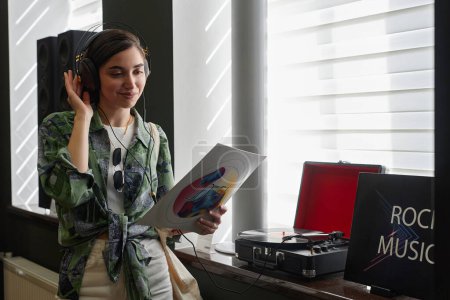 Téléchargez les photos : Portrait taille haute d'une jeune femme souriante écoutant des disques vinyle dans un magasin de musique, espace de copie - en image libre de droit