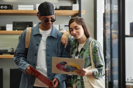 Téléchargez les photos : Portrait taille haute d'un jeune couple souriant choisissant des disques vinyle dans un magasin de musique - en image libre de droit