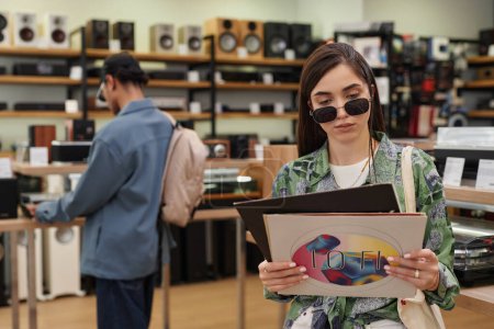 Téléchargez les photos : Portrait taille haute de jeune femme tenant un ensemble de disques vinyle dans un magasin de musique, espace de copie - en image libre de droit