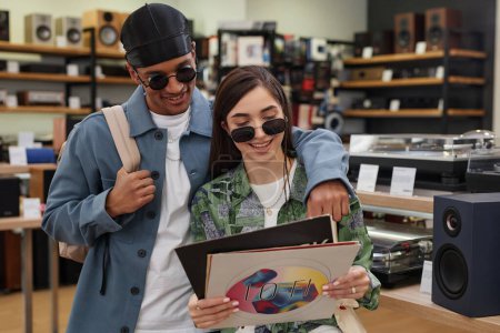 Foto de Cintura hacia arriba retrato de pareja joven multiétnica sosteniendo discos de vinilo en la tienda de música y sonriendo - Imagen libre de derechos