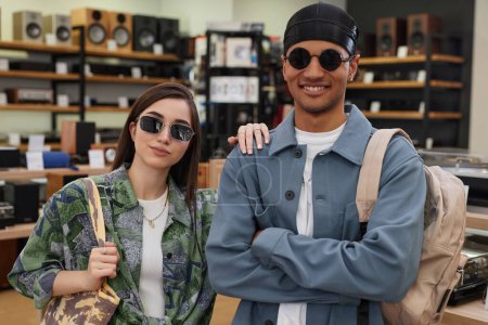 Photo for Waist up portrait of funky young couple wearing sunglasses while standing in music store and looking at camera - Royalty Free Image