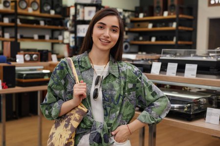 Photo for Waist up portrait of smiling young woman standing in music store and looking at camera - Royalty Free Image