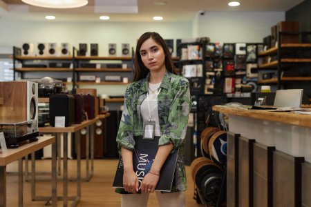 Portrait of young woman working in music store amd holding vinyl record looking at camera, copy space