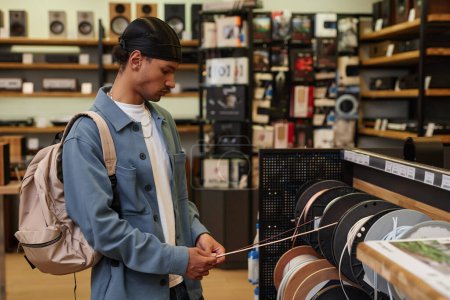 Foto de Retrato de vista lateral del joven negro eligiendo cables y cordones para equipos de música en la tienda, espacio de copia - Imagen libre de derechos