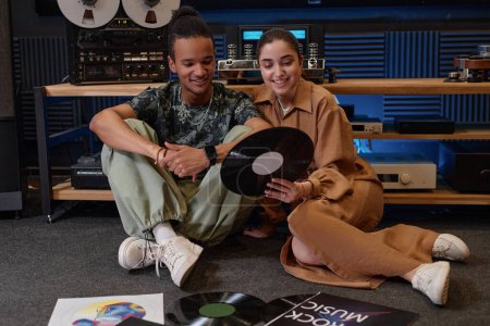 Téléchargez les photos : Portrait of smiling young couple choosing vinyl records from home collection sitting on floor together - en image libre de droit