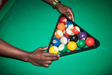 Photo for Close up of unrecognizable Black man setting billiard balls in triangle frame on green pool table shot with flash copy space - Royalty Free Image