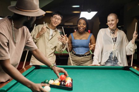 Téléchargez les photos : Groupe diversifié de jeunes gens joyeux jouant au billard ensemble debout table ronde - en image libre de droit