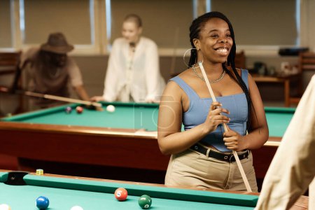 Photo for Waist up portrait of smiling African American woman chatting with friend while enjoying game of pool together in low light copy space - Royalty Free Image