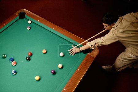Photo for Minimal top view of Asian man playing billiards and hitting ball with cue stick copy space - Royalty Free Image