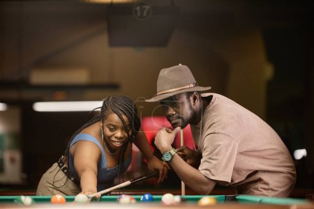 Téléchargez les photos : Portrait d'un couple afro-américain adulte jouant au billard ensemble et se penchant sur la table dans une boîte de nuit - en image libre de droit