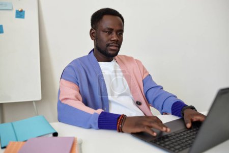 Foto de Retrato de hombre negro creativo usando el ordenador portátil en la oficina y el uso de ropa de colores, espacio de copia - Imagen libre de derechos