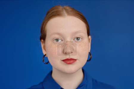 Téléchargez les photos : Vibrant portrait en gros plan de jeune femme rousse regardant la caméra sur bleu, espace de copie - en image libre de droit