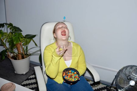 Foto de Retrato de mujer joven divirtiéndose en el trabajo y comiendo dulces coloridos lanzándolo al aire, espacio para copiar - Imagen libre de derechos
