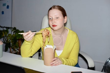 Téléchargez les photos : Portrait de jeune femme mangeant des nouilles à emporter à l'intérieur, prise de vue avec flash - en image libre de droit