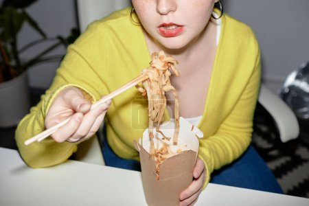 Téléchargez les photos : Gros plan de jeune femme mangeant des nouilles à emporter à l'intérieur, prise de vue avec flash - en image libre de droit