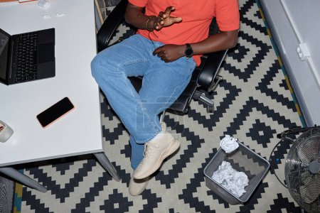 Foto de Vibrante plano de vista superior del hombre negro arrojando papel en la cesta en el lugar de trabajo, espacio de copia - Imagen libre de derechos