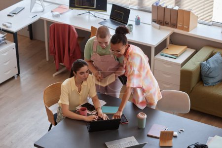 Draufsicht auf eine Gruppe junger Frauen, die gemeinsam im modernen Büro arbeiten und Laptop und Kopierraum nutzen