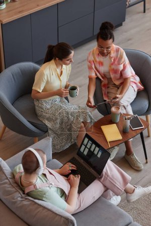 Draufsicht auf drei junge Frauen, die sich mit Laptop treffen, während sie gemeinsam an einem IT-Projekt arbeiten
