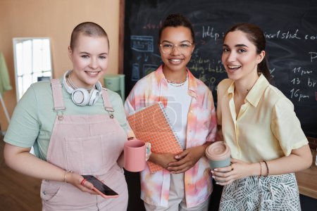 Waist up portrait of diverse team of three young women smiling at camera standing in modern office