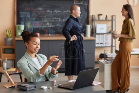 Téléchargez les photos : Portrait d'une femme d'affaires noire souriante faisant une manucure sur le lieu de travail avec toute l'équipe féminine au bureau, espace de copie - en image libre de droit