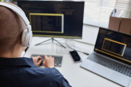 Photo for Back view of bald young woman wearing headphones and using computer while writing code and working in IT, copy space - Royalty Free Image