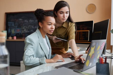 Foto de Retrato de vista lateral de dos mujeres jóvenes que usan el ordenador portátil juntas mientras revisan el código y el proyecto de TI - Imagen libre de derechos
