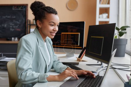 Photo for Side view portrait of young black woman programming code and using computer in office - Royalty Free Image