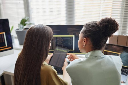 Vista posterior a dos mujeres jóvenes sosteniendo tableta digital con código