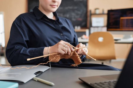 Closeup of gen Z young woman knitting or crocheting at workplace in office, copy space