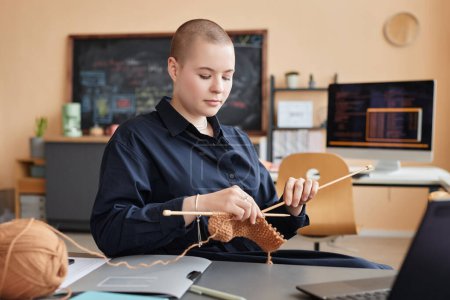 Portrait of gen Z young woman knitting or crocheting at workplace in office