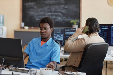 Téléchargez les photos : Jeune ingénieur sérieux en cybersécurité regardant l'écran d'ordinateur assis par le lieu de travail et analysant les données contre un collègue masculin - en image libre de droit