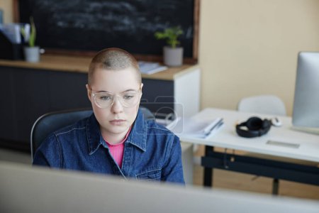 Junge ernsthafte IT-Managerin mit Brille blickt am Arbeitsplatz im Büro auf den Computerbildschirm und arbeitet mit grafischen Daten