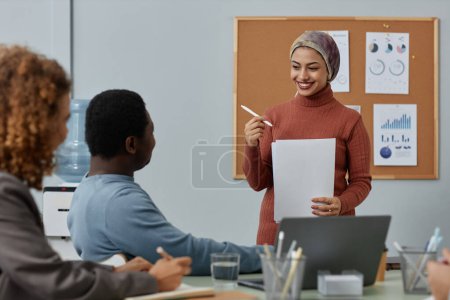 Photo for Young successful female broker with papers looking at African American male colleague while standing in front of audience during report - Royalty Free Image