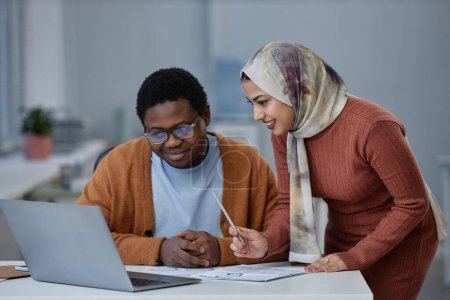 Junge Vertrauensperson weibliche Ökonomin oder Analystin erklärt Präsentation Punkt zu männlichen Kollegen bei Treffen, während beide auf Laptop-Bildschirm schauen