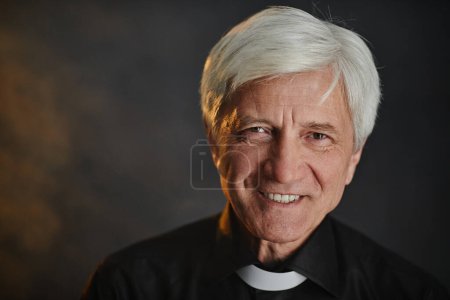 Foto de Primer plano retrato de un sacerdote mayor de pelo blanco mirando a la cámara con sonrisa, espacio para copiar - Imagen libre de derechos