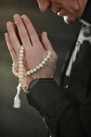 Photo for Vertical side view portrait of senior priest with hands clasped in prayer and rosary - Royalty Free Image