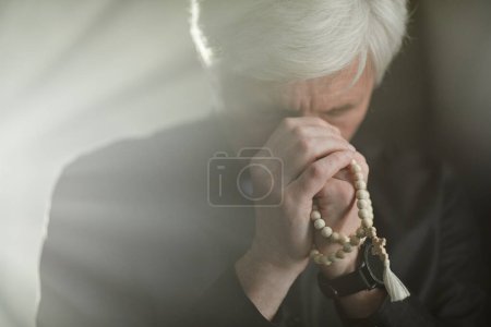 Foto de Vista frontal del sacerdote mayor de pelo blanco rezando con rosario en serenos rayos de dios, espacio para copiar - Imagen libre de derechos