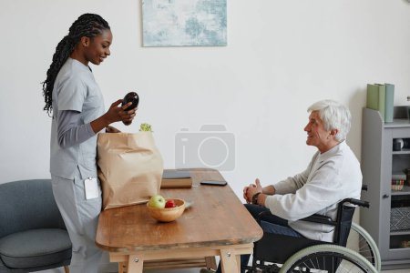Photo for Side view portrait of nurse delivering bag with groceries to senior man with disability - Royalty Free Image