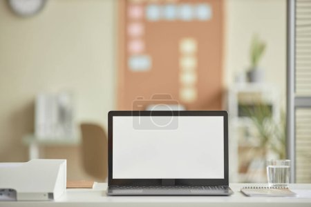 Téléchargez les photos : Image de fond minimale de l'ordinateur portable ouvert avec maquette d'écran blanc vierge sur le bureau dans le lieu de travail de bureau, espace de copie - en image libre de droit
