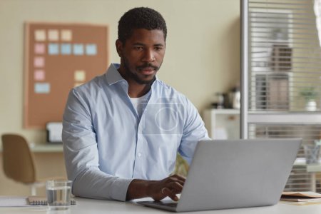 Téléchargez les photos : Portrait d'un bel homme noir en homme d'affaires utilisant un ordinateur portable au bureau, espace de copie - en image libre de droit