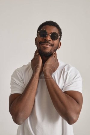 Foto de Retrato mínimo del hombre afroamericano con gafas de sol posando en estudio contra blanco - Imagen libre de derechos