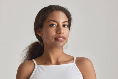 Photo for Closeup portrait of young African American woman looking at camera against white, simple beauty - Royalty Free Image
