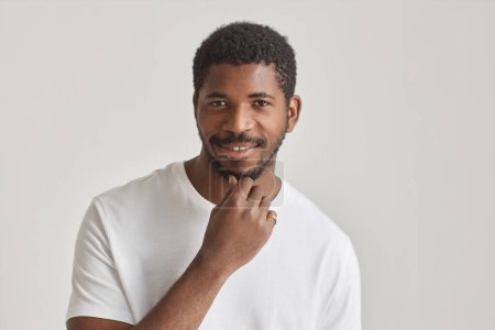 Photo for Minimal portrait of confident black man smiling at camera against white background and stroking beard - Royalty Free Image