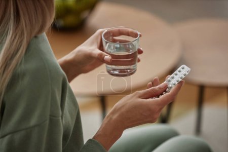Téléchargez les photos : Gros plan d'une jeune femme méconnaissable prenant des médicaments à la maison et tenant un verre d'eau - en image libre de droit